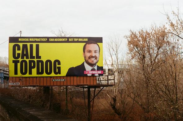 A billboard shouts at its audience “CALL TOP DOG” with some regular schmo lawyer with a shit resting grin on his face