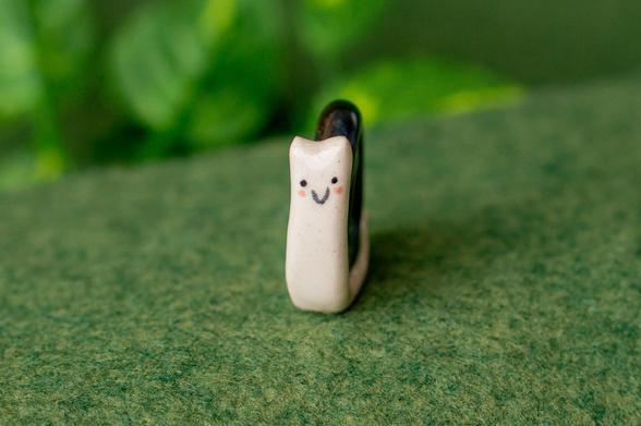 A tiny ceramic snail with a cute cartoonish smiling face, facing the camera.
