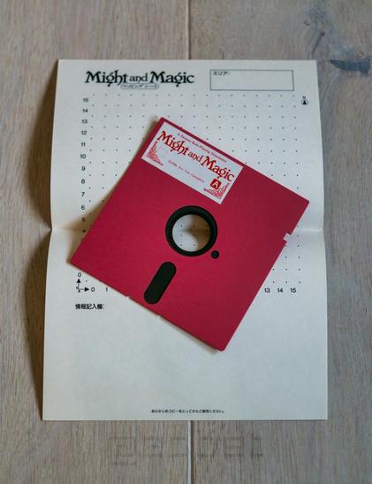A red 5.25 floppy disk from the Japanese release of the first Might & Magic on top of official graph paper from the same box.