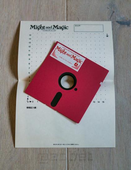 A red 5.25 floppy disk from the Japanese release of the first Might & Magic on top of official graph paper from the same box.