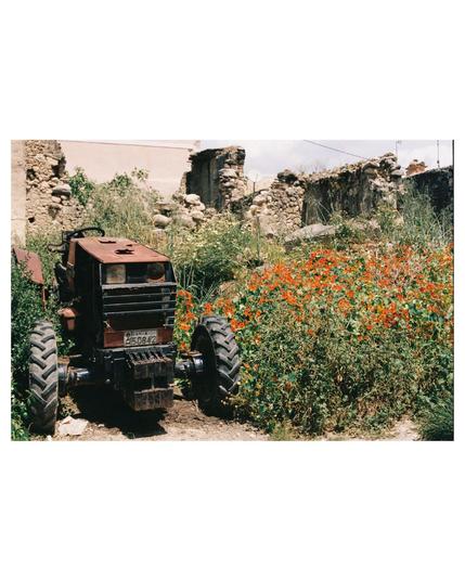 old tractor surrounded by ruins of old stone houses. Everythings overgrown by wild flowers