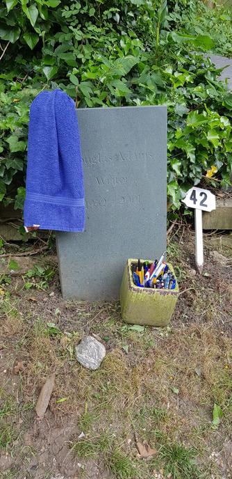 Douglas Adams' grave with blue towel on the gravestone in 2018.

Next to it is a sign with 42 on it and a box of pens