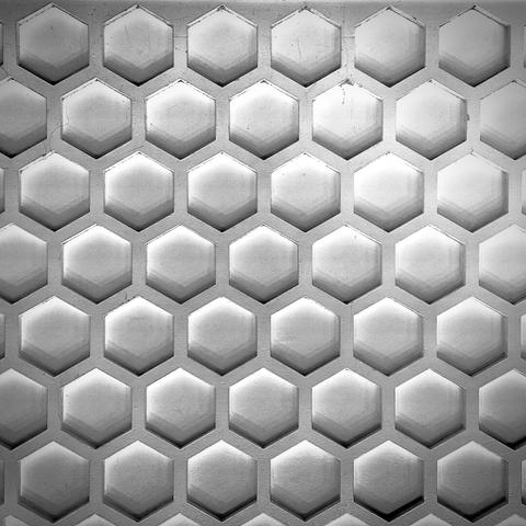 A white, wooden, recessed hexagonal pattern fills the frame, lit from below by an unseen light source.