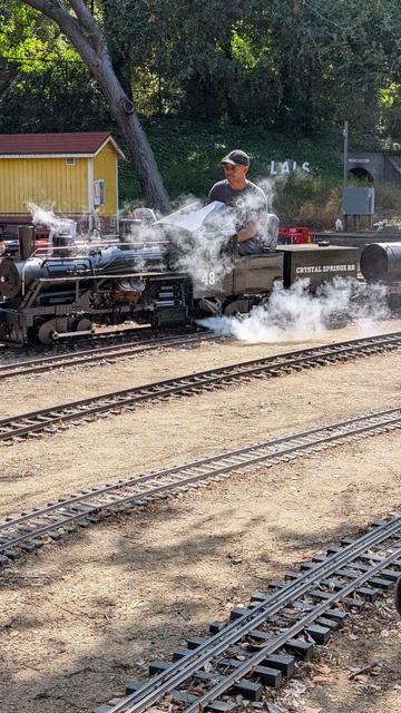 A large ride-on Shay locomotive spews steam everywhere as it chugs on by