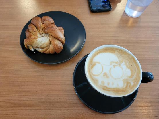 A pastry and a coffee with a skull shape as the foam art.