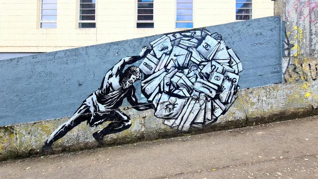 A mural of a man pushing a rock made of modern brands up a steep hill.