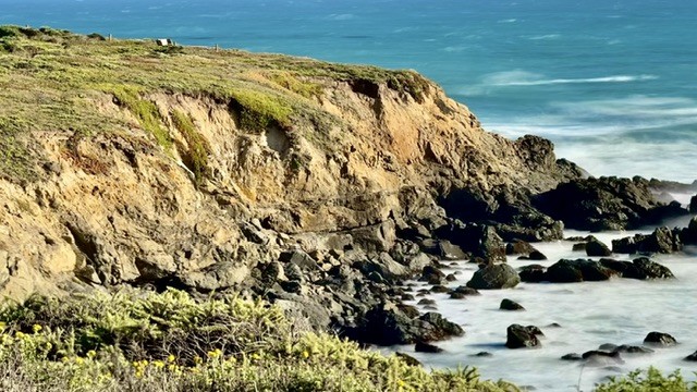 This is a view of the seacoast from Fiscalini Ranch in Cambria California. It is rendered using the iPhone Live photo feature called Long Exposure. The image shows the ocean with the waves turned into ethereal mist, while the rocky coast with wildflowers is sharp (except where the wind moved the plants and that's blurred).