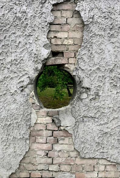 concrete and brick wall with circular hole, with grass and a tree visible though it - Photo by Mihály Köles on Unsplash