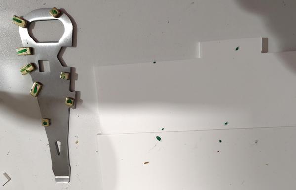 Silver can opener with golden magnets with green markings and white plastic parts with green markings on a workbench