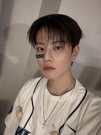 Selfie of Seungmin in a white t-shirt with a band-aid on his face, wearing a silver chain with a cross pendant