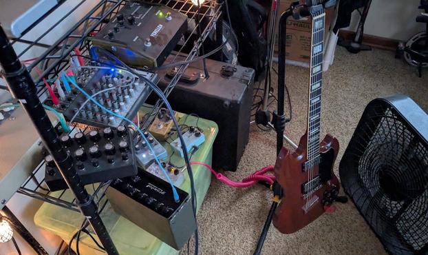 a bunch of musical equipment wired to make drones - a couple of drone synths, some effects pedals, a mixer, and a guitar with a box fan blowing across the strings.