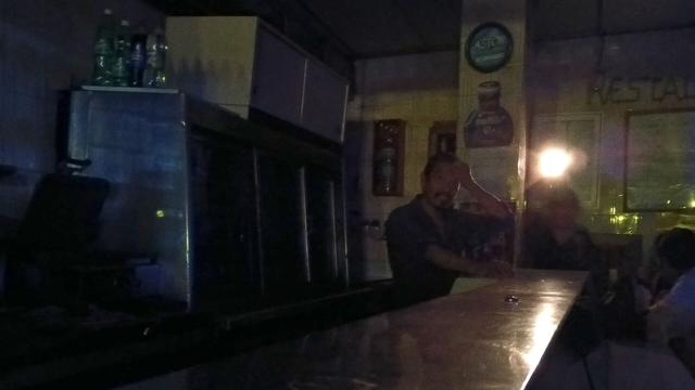 A photo of a group of people hanging at a bar during a blackout. A man is walking on the back holding a flashlight.
