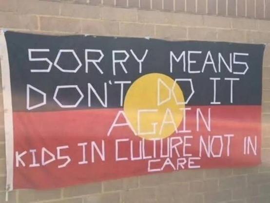 The Aboriginal flag, with text over it:
SORRY MEANS DON'T DO IT AGAIN 
KIDS IN CULTURE NOT IN CARE