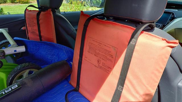 End-of-life throwable personal flotation devices repurposed as protective seat back covers in an automobile with cargo behind front seats.
