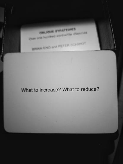 A black-and-white photo of an Oblique Strategy card. The card reads: 'What to increase? What to reduce?'.