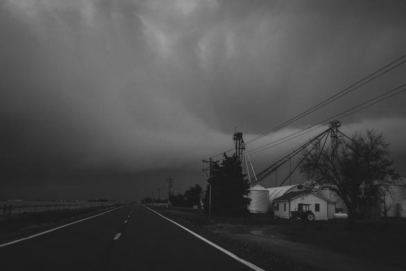 Storm coming over the horizon on a country road. A group of silos on the right side.