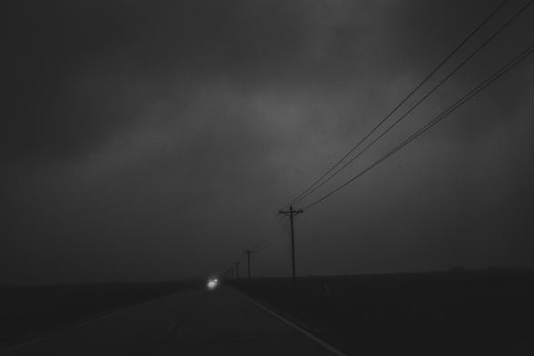 The storm has come and the scene is dark and ominous. Headlights approach in the distance.