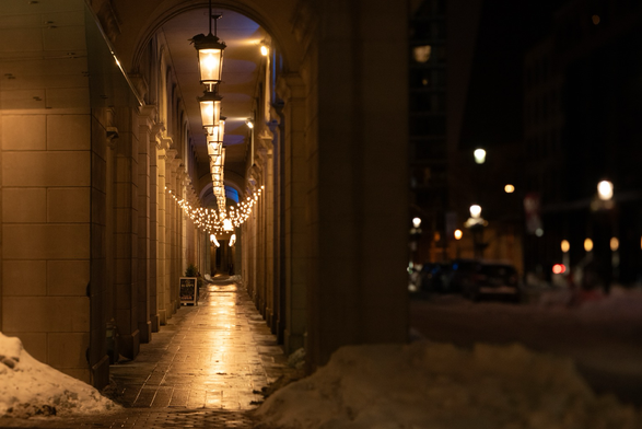 A view down a long and well lit colonnade on a winter night, snow is piled next to the entrance.