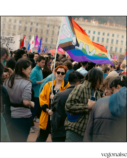 photo de manif où une personne au milieu de la foule affiche un drapeau progress avec le logo du STJV (syndicat des travailleureuses du jeu vidéo)
