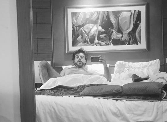 Selfie in the mirror of the cabin in the cruise. In black and white, staring at the camera from the bed. Hairy chested and fussy hair.