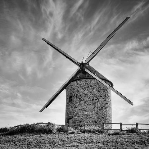 Eine alte Windmühle in der Normandie, die ich von schrägunten nach oben fotografiert habe. Im Hintergrund sieht man den Himmel mit Schleierwolken.  Das Foto ist in Schwarzweiß.