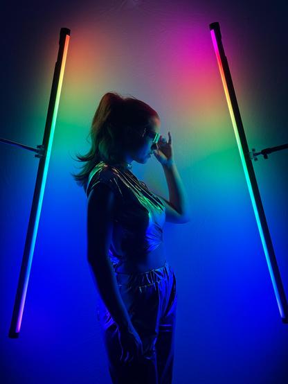 A striking silhouette of a female model standing between two vertical neon lights with a rainbow gradient backdrop, creating a dramatic and vibrant visual effect