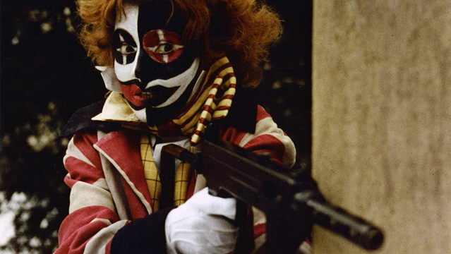 Movie character with a contrasted b/w mask, extravert theatrical costume, white gloves and a gun.