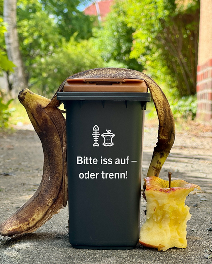 Miniatur-BSR-Biotonne. Darauf steht: Bitte iss auf - oder trenn! Über der Tonne liegt eine Bananenschale und daneben steht ein Apfelgriebsch