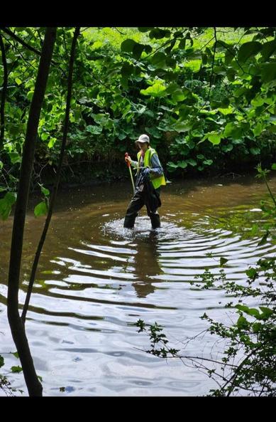 Picture of myself in a pair of waders and a Hi Vis vest in the water up to my knees with trash bag in one hand a pole in the other