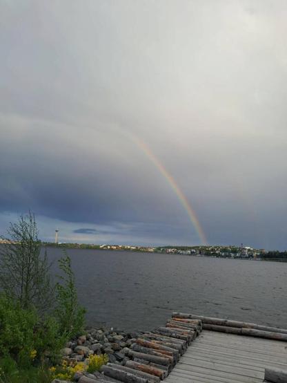 Näkymä Näsijärven yli Tampereelle. Etualalla laituri, taivaalla sateenkaari. Vasemmalla Näsinneula, oikealla Pispalan haulitehdas. Taivas on pilvinen, mutta aurinko osuu osaan kaupunkia