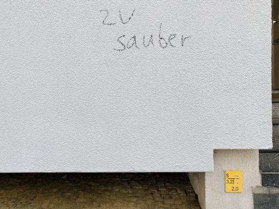 Frisch geweißte Hauswand, auf der mit schwarzer Kreide »zu sauber« geschrieben steht.
