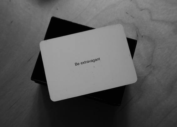 A black-and-white photo of an Oblique Strategy card. The card reads: 'Be extravagant'.