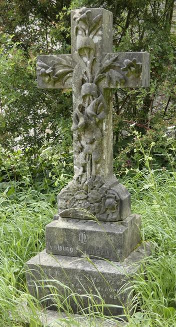 An ornate stone cross gravestone amid willd grass