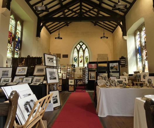 Loking up the nave of a small church with stained glass windows either side and over the alter. An art exhibition fill the space