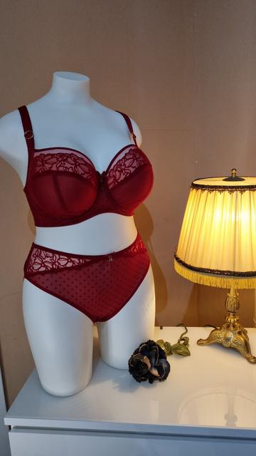 Eine Puppe trägt ein rotes Spitzen Set. Der BH und der Slip sind mit rotem Blumen-Samtprint und Samtpunkten. Der BH ist am Dekolleté transparent mit roten Abschlüssen, so dass es so wirkt, als hätte der BH Bänder.