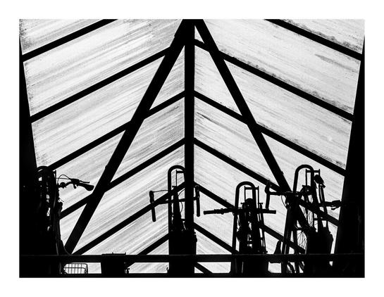 a shot from below towards a transparent roof of a bike parking in a railway station. The supporting structure is clearly visible with triangles and diagonal beams holding up the transparent plastic roof, which is sprinkled with dots. On the bottom there are some bicycle silhouettes.