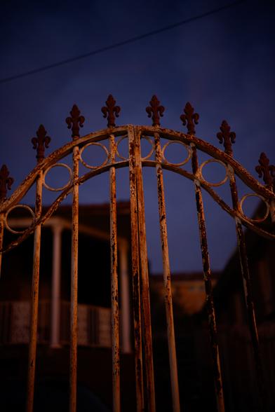 A rusty iron gate in orange light with a dark blue evening sky background