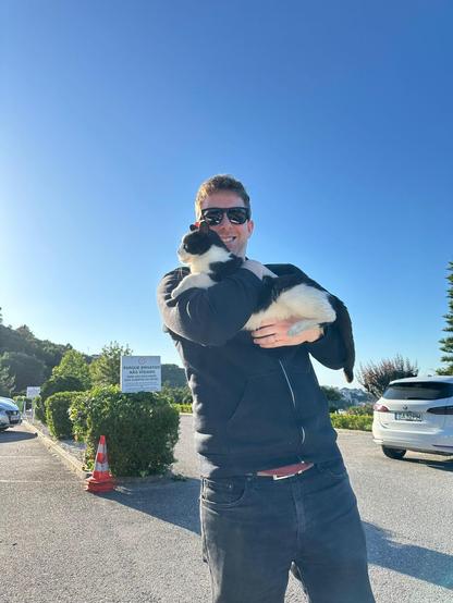 Me in sunglasses, smiling, holding up the cute black and white cat