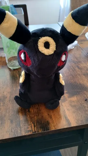Self-sewn Umbreon plushie sitting on a desk. It's looking at the camera