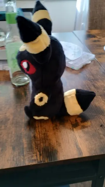 Sideview of the self-sewn Umbreon plushie sitting on a desk. It's looking to the left