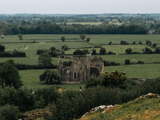 a ruin surrounded by a grassy field and hedgerows