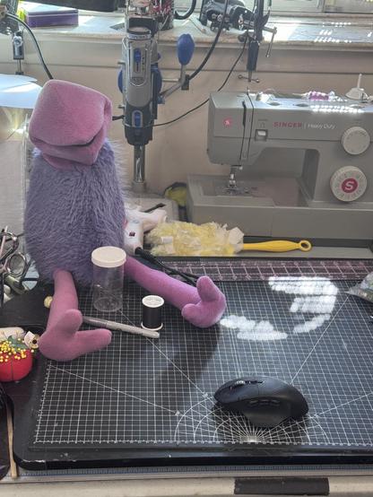 A pink and purple puppet under construction on a work table with a sewing machine and other tools