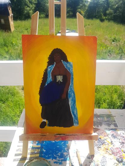 Peinture acrylique d'une personne qui pose sur un fond jaune et orange.
La personne a les cheveux très longs et curly, la peau noire, regarde sur le côté avec une moue.
Iel porte un corset noir peind d'une cage thoracique, une cape bleu océan avec des vagurs, une jupe volumineuse bleu nuit et une longue jupe noir. Iel montre sa cheville et son pied droit. On voit son torse nu.

Le chevalet est posé sur une table sur le balcon avec vu sur un jardin en friche
