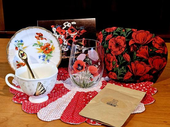 Tea tableau in red with a theme of poppies as depicted on china, linens, glass, and artwork on a quilted doily. The tea is loose-leaf Cherry black tea.
