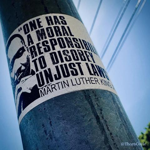 A sticker on a metal pole, Sky and wires above:

“One has a moral responsibility to disobey unjust laws.”

— Dr. Martin Luther King Jr.