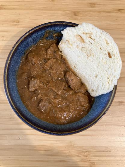 A bowl of beef stew with a slice of bread dumpling.