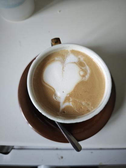 An old bar coffee cup, filled with a latte art attempt, you can make out the heart shape despite the various imperfections.