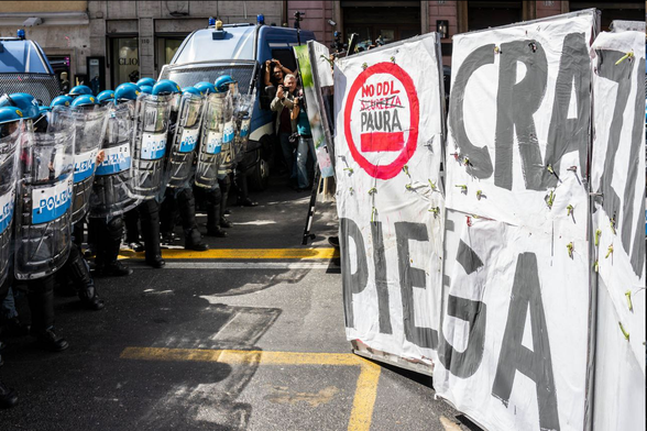 Faccia a faccia tra corteo e polizia antissommossa. Il corteo è dietro allo striscione “la democrazia non si piega", suddiviso in vari pannelli. Su uno: NO DDL PAURA.