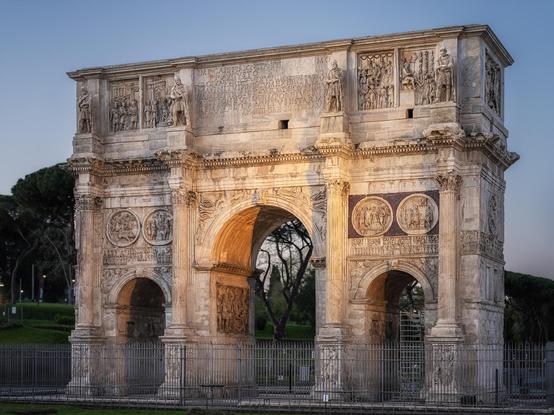 The Arch of Constantine in Rome Italy, shown in the early morning light. It was built in 315 CE and has 3 archways, the middle one larger than the out two. There are inscriptions in the 'attic' of the arch and carvings and reliefs ver the rest of the surface.