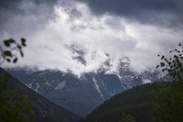 Mountain peaks partially shrouded in swirling clouds, with dark, forested slopes in the foreground.